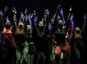 student dancers on a dark stage with arms raised overhead